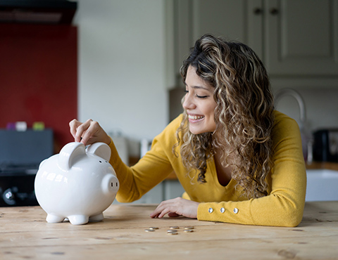 Young woman putting coins in piggy bank
